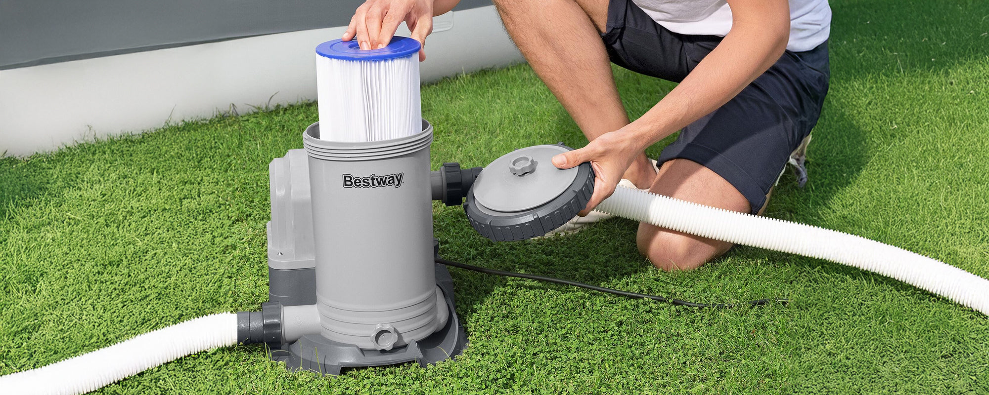 A close-up of a man bent down changing the filter cartridge in a gray Bestway cartridge filter pump. 