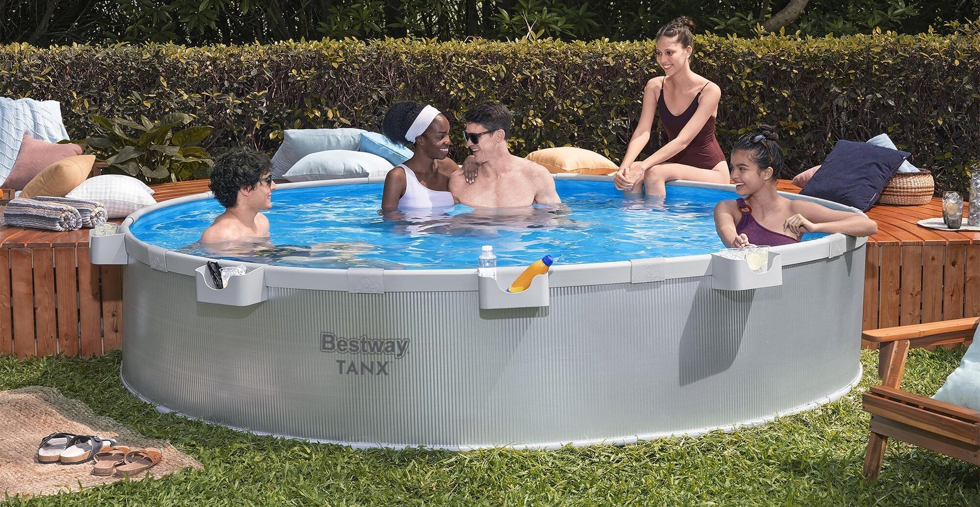 Five friends lounging in a Bestway TANX stock tank pool with drinks and essentials in the accessory cup holders.