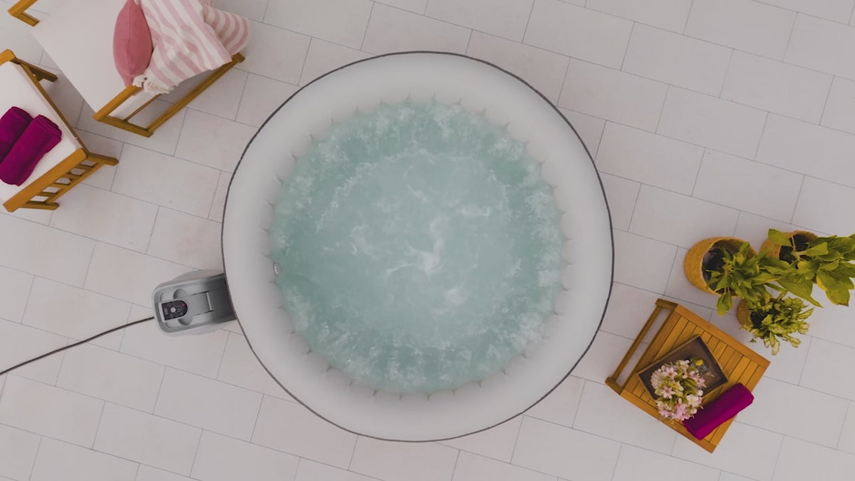 Load video: A promotional video showcasing a grey, inflatable SaluSpa hot tub. It features scenes of the bubbling hot tub on a patio, a woman checking the water temperature, underwater jets creating vigorous bubbles, and couples happily relaxing, smiling, and toasting drinks inside the hot tub.
